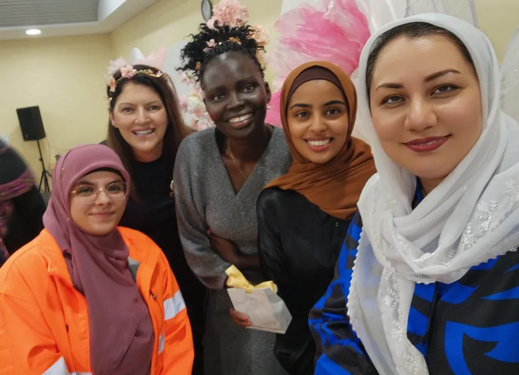 Five women smiling together at an indoor event